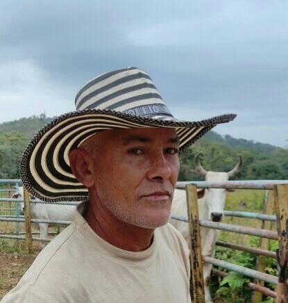 Rotro de Arcenio Lópezcon sombrero, al fondo un potrero  donde un toro de color blanco mira a la cámara